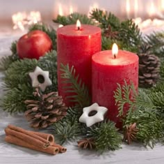 three red candles surrounded by pine cones, cinnamon sticks and other christmas decorations on a table