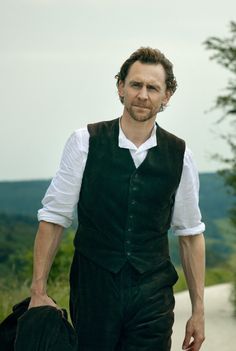 a man in a vest and tie walking down a road