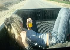 two people sitting in the back of a pick up truck drinking from a beer bottle