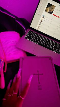 a laptop computer sitting on top of a desk next to a pink book and pen