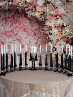 a table topped with lots of candles next to a wall covered in pink and white flowers