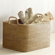 a basket filled with firewood sitting on top of a wooden floor next to a white wall