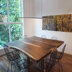 a wooden table surrounded by four chairs in front of a large window with trees outside