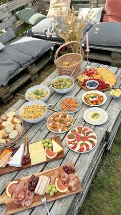 an outdoor picnic table filled with cheeses, meats and fruit on wooden boards