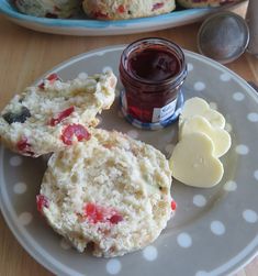 two scones with jam and butter on a plate next to some other pastries