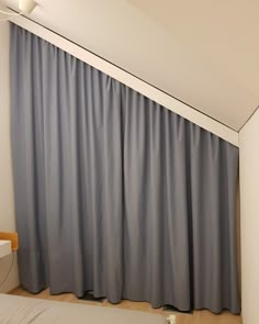 a bed sitting under a window next to a gray curtain in a room with white walls