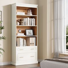 a white bookcase with books on it in a bedroom next to a large window