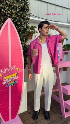 a man standing next to a pink surfboard