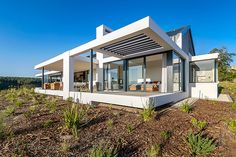 a modern house on top of a hill with lots of grass and bushes around it