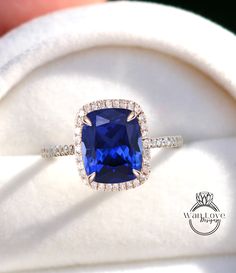 a cushion cut blue sapphire surrounded by diamond halos on a white cloth ring box