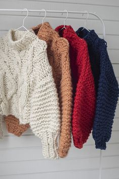 four knitted sweaters hanging on a white hanger in front of a wall