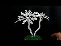 a hand holding a small white tree on top of a green base with snow flakes