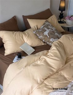 an unmade bed with a book and some pillows on top of it, next to a lamp