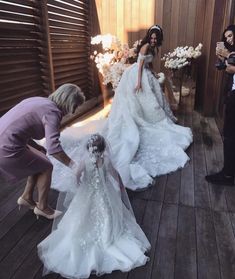 two women in wedding gowns and one man taking pictures with her phone on the deck