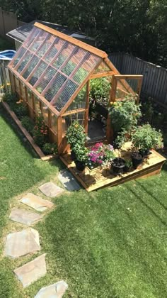 a small greenhouse in the middle of a yard with flowers and plants growing inside it