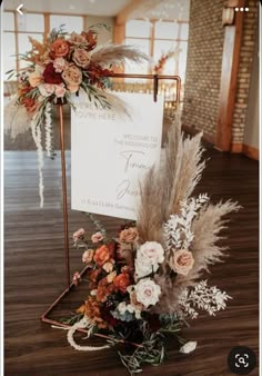 an arrangement of flowers and feathers on display in front of a welcome sign at a wedding