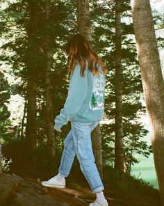 a woman walking on a log in the woods with trees behind her and back to the camera