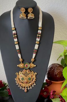 An elegant set for your local gatherings or parties. The length of the pendant necklace is given in one of the pictures. Measurements of the jhumkas. Height: 4 Cm  Width : 2.5 Cm  Care Instruction : Avoid Heat & Chemicals Like Perfume, Deo, Alchol, Etc. | Clean With Dry Cotton Cloth | Pack In our Anti tarnish box after use. Pearl Necklace With Latkans For Festivals, Festive Pearl Necklace With Latkans As A Gift, Traditional Festive Jewelry Set With Pearl Pendant, Festive Traditional Jewelry Set With Pearl Pendant, Traditional Festive Jewelry Sets With Long Necklace, Traditional Long Temple Necklace For Celebration, Traditional Jewelry Sets With Long Necklace For Celebration, Temple Necklace With Pearl Chain As Diwali Gift, Traditional Long Necklace Jewelry Sets For Celebration