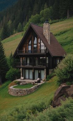 a house on a hill with trees in the back ground and green grass around it