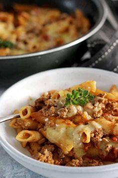 two bowls filled with pasta and meat covered in sauce on top of a marble table