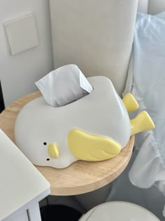 a white and yellow whale shaped tissue dispenser on a wooden table next to a bed