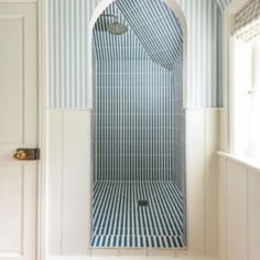 a bathroom with blue and white stripes on the walls, shower stall and toilet in the corner