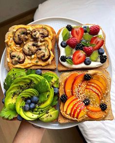 a person holding a plate with fruit and sandwiches on it