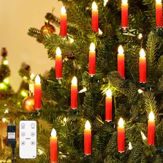 a christmas tree with many lit candles on it and a remote control in the foreground