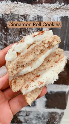 a hand holding a piece of cake with icing and cinnamon on it, in front of a brick wall