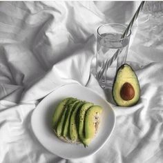 an avocado cut in half on a plate next to a glass of water