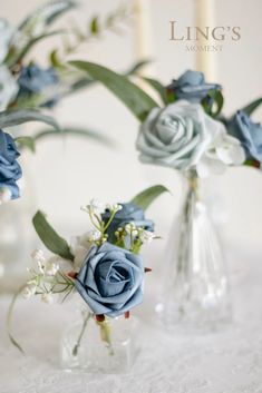 two vases filled with blue flowers on top of a white table covered in lace