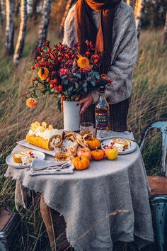 a woman standing next to a table filled with food and flowers on top of it