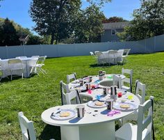 a table set up with plates and cups for an outdoor party in the grass near a fence