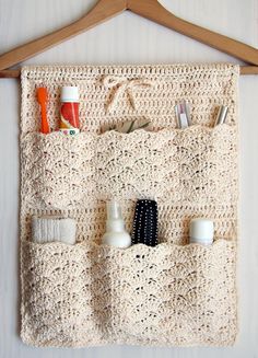 a crocheted purse hanging on a wooden hanger with toothbrushes and other items in it