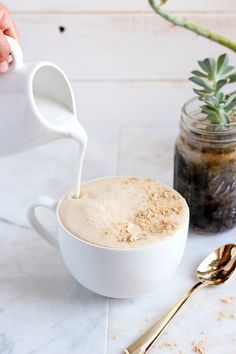 a person pours milk into a bowl with a spoon on a table next to a potted plant