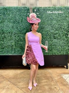 a woman standing in front of a green wall wearing a purple dress and pink hat