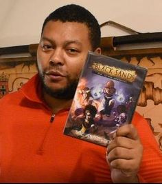 a man in an orange shirt holding up a video game box with the title black sand on it