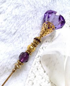 "8.1/2\" HATPIN with Large Dark PURPLE Crystal Shape and Round Faceted Crystal on Gold Finish Setting. The Large Faceted Purple Bead on Top is 7/8\"x 3/4\", in the Center a Purple Rhinestones Roundel and at the base, a Round Faceted Crystal 3/8\" diameter, all set  Gold Finish Findings.  THE DECORATED AREA IS  2.7/8\" ON THE 8.1/4 INCH HATPIN. MADE OF STAINLESS  VERY CLASSY TO WEAR, ADD IT TO YOUR COLLECTION OR OFFER AS A GIFT. OUR HATPIN SHIP WITH A METAL SAFETY END. The rod is sturdy made of 15 Gauge Brass. ------------------------------------  * Hand crafted in the U.S.A.  * Limited edition hatpins, not mass produced abroad.   * Payment must be received in 10 days.  * Dotty is now Retired and a graduate from The Maryland Institute of Art and meticulously creates these hatpins with parts Wand Ideas, Dark Purple Crystal, Fairy Shoes, Pretty Knives, Pretty Jewelry Necklaces, Purple Jewelry, Anime Accessories, Magical Jewelry, Crystal Shapes