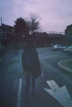 a woman standing in the middle of an empty parking lot at dusk with her umbrella up