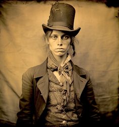 a sepia photograph of a woman wearing a top hat and jacket with an odd look on her face