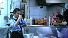 a man standing in front of a counter talking on a cell phone while holding a drink