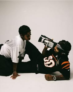 two young men sitting on the ground with cameras in their hands