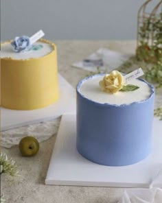 two cakes are sitting on a table, one is blue and the other is yellow