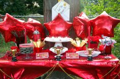 a table topped with red balloons and desserts next to a forest filled with trees