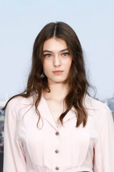 a woman with long brown hair wearing a pink shirt and black belted skirt standing in front of a cityscape