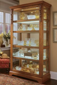 a wooden display case filled with lots of glassware on top of a rug next to a window