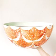 a hand holding a bowl with an orange design on the bottom and white rim, in front of a white background