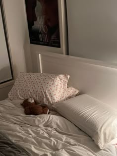 a teddy bear laying on top of a bed with white sheets and pillows in a bedroom