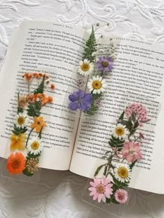 three bookmarks with flowers on them are placed next to an open book that is sitting on a table