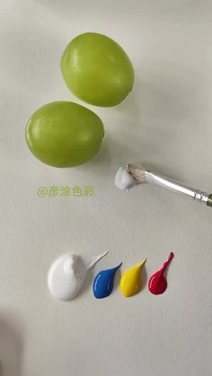 three different colors of paint next to an artist's brush and two green eggs